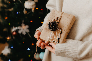 girl holding small gift in her hands. decorated Christmas tree on background. Bright Christmas card with space for text