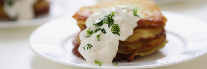 Potato pancakes with sour cream and herbs on plate closeup