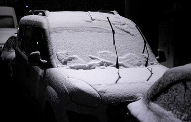 Car windshield wipers left up against freezing in snow. Night view of winter conditions.