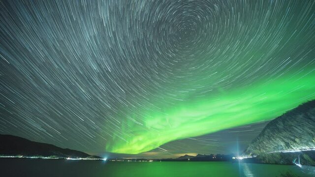 Starry sky and northern lights above the fjord. City lights in a distance. Full night timelapse.