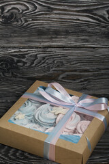 Marshmallow blue and pink. Lies in craft packaging. Decorated with mastic snowflakes. The box is tied with a ribbon tied to a bow. On black pine boards.