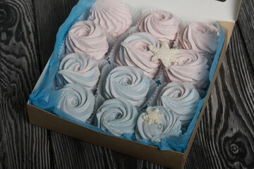 Marshmallow blue and pink. Lies in craft packaging. Decorated with mastic snowflakes. On black pine boards.
