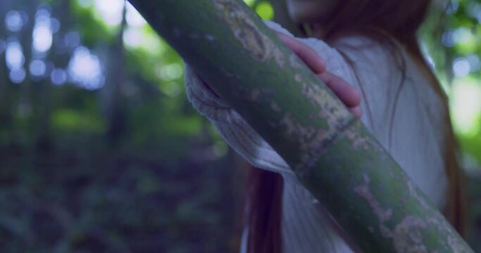 Young girl slides her hand on a bamboo tree with her face blurred in the background