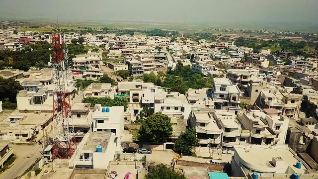 Top down aerial view of small houses in sunny weather with grassy fields  and roads , traffic. Camera is raising up over bulidings in mIrpur Azad Kahsmir, Pakistan