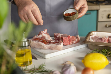 Staying at home and cooking. Man in the kitchen cuts meat, prepares food, adds spices and salt.