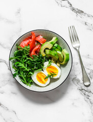 Delicious healthy breakfast, snack - boiled egg, avocado, arugula and smoked salmon in one plate on a light background, top view