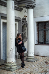 Fototapeta na wymiar stylish brunette in a black coat and black shoes breathes autumn air in a strange city
