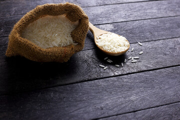 Spoon of uncooked rice and sag of rice grain on black