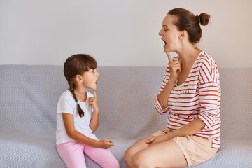 Profile shot of woman physiotherapist having lesson with small child girl for correct articulation,...