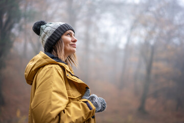 Attractive young woman in yellow park and hat enjoying fresh air in autumn foggy forest