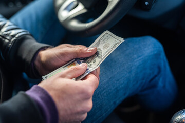 hands of a car driver holding banknotes of dollars in the middle in the car.
