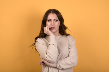 A scared and worried Caucasian brunette girl with wavy hair in a casual jumper holding her hand to...