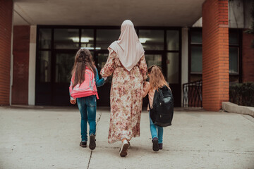 Hijab muslim mother walking her kids to school. Selective focus