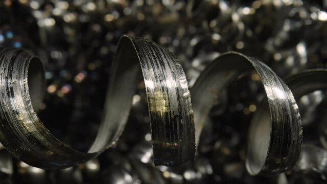 Curly metal chippings after end milling. Macro shot of sharp spirals of silver colored metal. Waste aluminium shavings. Camera pans inside pile of waste metal shavings in slow motion. Close up.