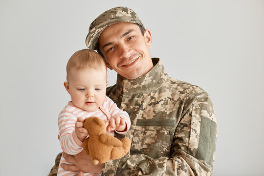 Portrait of happy positive father came from the war or the army exercises and holding his charming baby, looks cute, expressing love, missing his family during military serve. - Powered by Adobe