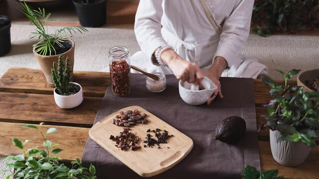 Woman hands putting chili pepper, solt in organic cacao, cooking on table, cocoa nibs, beans, artisanal chocolate making in rustic style for ceremony. Chocolate making with pounder close-up top view