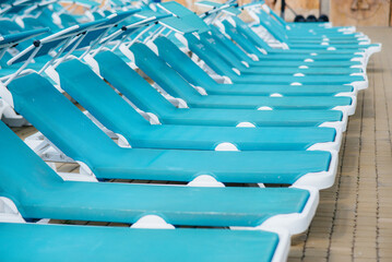 A lot of new beautiful blue sun loungers are standing near the pool in the hotel on a sunny day. Happy vacation vacation. Summer holidays and tourism.