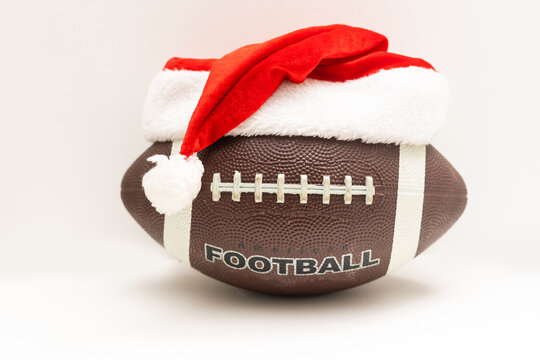 A Souvenir Ball For Rugby Or American Football In A Red Santa Claus Hat On A Green Background. Preparation For Design Of Tickets, Posters, Postcards Or Business Cards On The Subject Of The Sports.