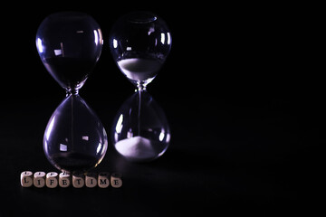 Sand running through the bulbs of an hourglass measuring the passing time in a countdown to a deadline, on a dark table background with copy space.