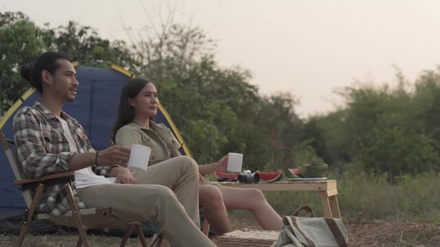 Tourists are happy and relaxed on vacation. Asian couple enjoying drink and nature while camping. Recreation travel and camping concept.