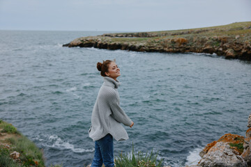 Fototapeta na wymiar woman in a gray sweater stands on a rocky shore nature Lifestyle
