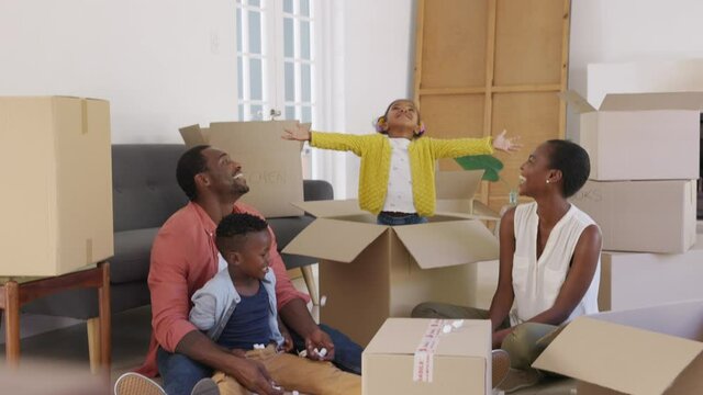 Happy african american family playing in new house with box filling material