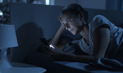 Woman lying in bed at night and connecting with her phone