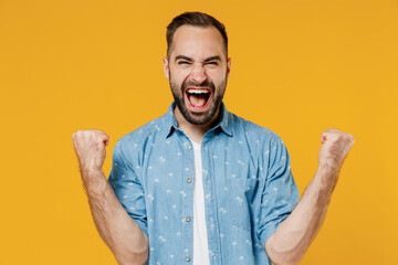 Young smiling happy caucasian man 20s wearing blue shirt doing winner gesture celebrate clenching...