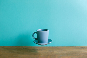 Gray coffee cup floating on wooden table. mint blue wall background