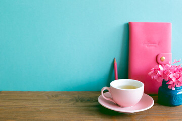 Pink diary, pencil, cup of tea, dry flowers on wooden table. mint blue wall background
