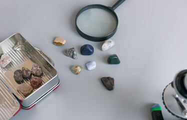 collection of semiprecious stones on gray table with magnifying glass, box and microscope. Mineral...