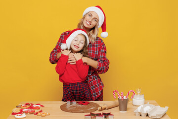Two woman mother fun child baby girl in red Christmas hat isolated on plain yellow wall background studio. Mom little kid cook ginger cookie at kitchen table home. Happy New Year 2022 holiday concept