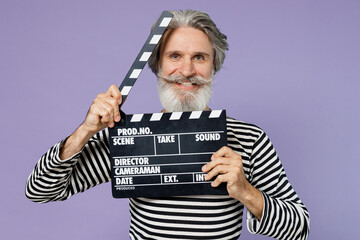 Elderly gray-haired mustache bearded man 50s wearing striped turtleneck holding classic black film making clapperboard isolated on plain pastel light purple background studio People lifestyle concept