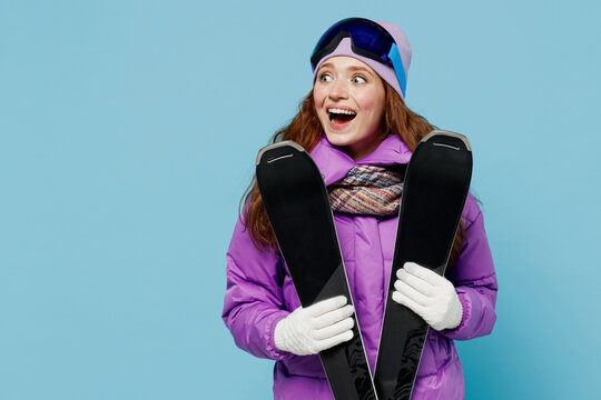 Skier surprised shocked happy woman in warm purple padded windbreaker jacket goggles mask spend extreme weekend in mountains hold ski look aside on workspace isolated on plain blue background studio