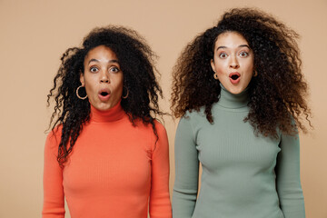 Two shocked fun young curly black women friends 20s wearing casual shirts clothes keeping mouth...