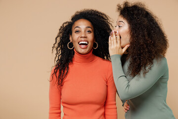 Two cheerful young curly black women friends 20s wearing casual shirts clothes whisper gossip and...