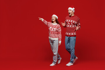 Full body young couple friends two man woman 20s in sweater hat walking going point finger aside...