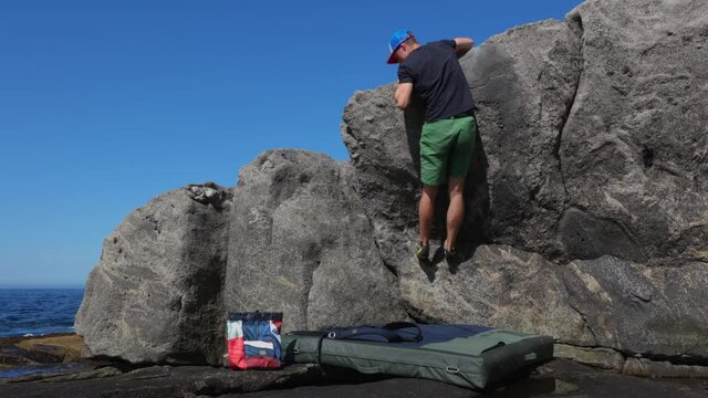 Young man bouldering on rocky beach with sea in background