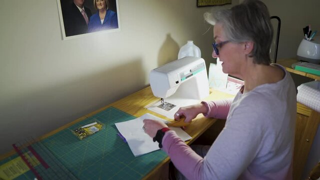 Mature woman making a quilt block with fabric squares in her sewing room