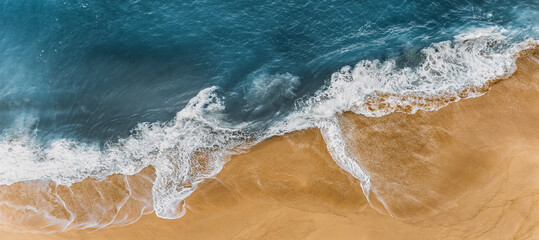 Panorama of a sandy beach with a wave rolling over it. Clean beach with yellow sand, panoramic view. Sea waves and sandy shore. Sea coast from a bird's-eye view, panorama. Clean seashore. Copy space