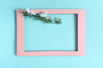 Pink paper frame decorated with white flowers with green leaves on a light background of apartments. Flat cardboard pink frame and decor of flowers and leaves