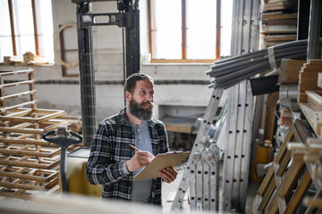 Mature male carpenter doing inventory indoors in carpentry workshop. Small business concept.