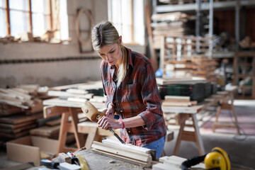 Portrait of female carpenter working on her product indoors in carpentry workshop.