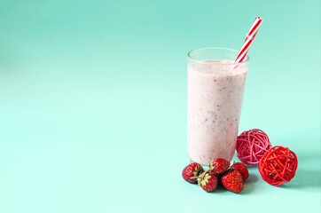 Milkshake in a transparent glass with raspberries and a red tube on a green background close-up. Cocktail of ice cream, milk and berries on a colored background copy space