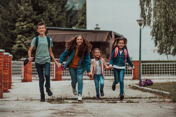 A group of students with protective masks on their faces run around the schoolyard while holding hands. Selective focus