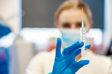 Close up of a nurse standing in a lab and holding a syringe with a corona virus vaccine. Any...