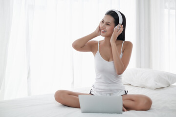 Asia woman sitting on the bed in morning with headphone and laptop