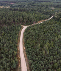 Areal drone view of gravel forest road. Both sides of road have trees.