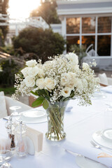 bouquet of white roses and gypsophila on a table on a white tablecloth with cutlery on the...