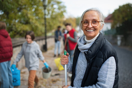 Senior woman volunteer with team cleaning up street, community service concept